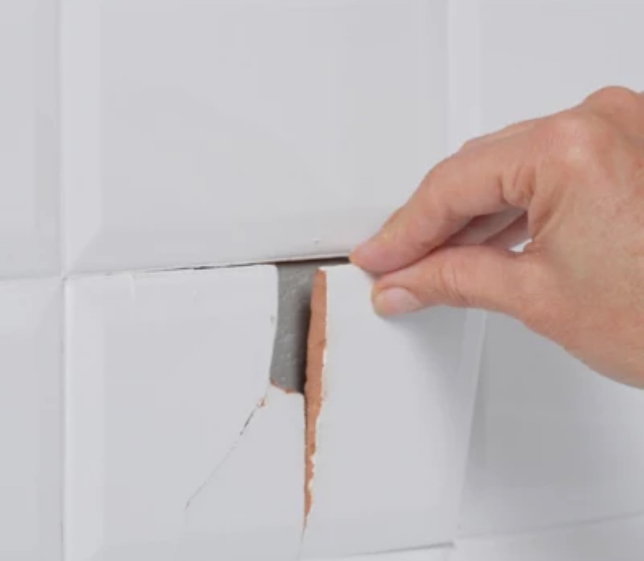Cracked wall tile being removed showing failed mortar bond — example of tile failure requiring root cause diagnosis
