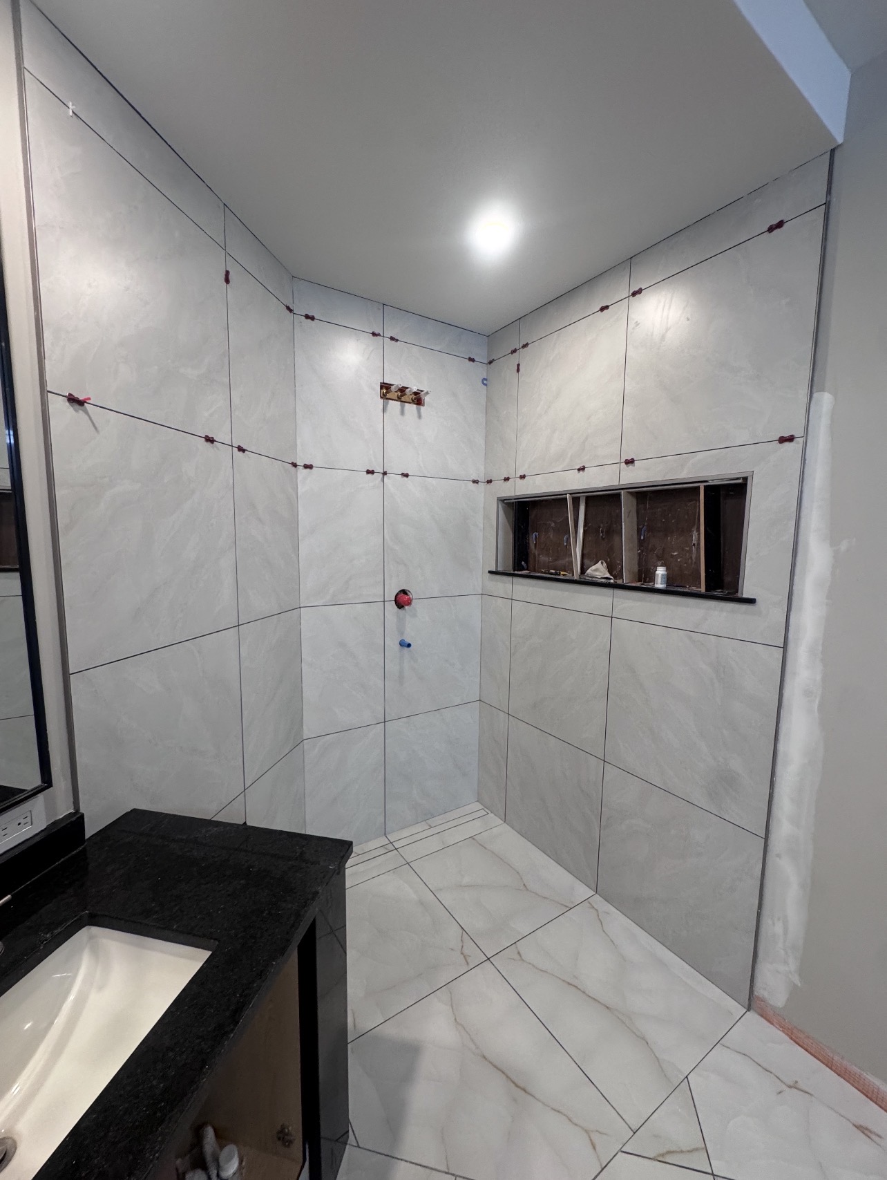 Large-format white tile shower installation in progress — leveling clips visible